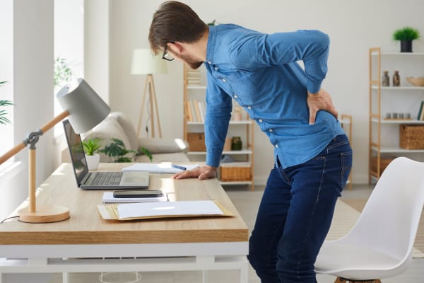 A man is standing in the office, experiencing low back pain.