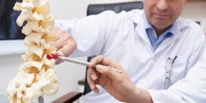 A spine specialist points to a spine model explaining the use of epidural steroid injection for pain relief.
