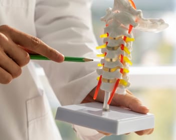A spine doctor explains the spine condition to a patient using a part of spine model.