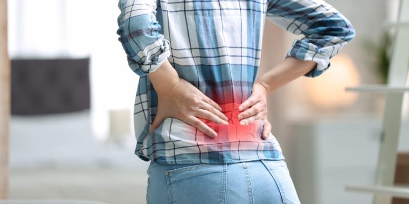 Woman holding her back in pain with red highlight indicating the painful area.