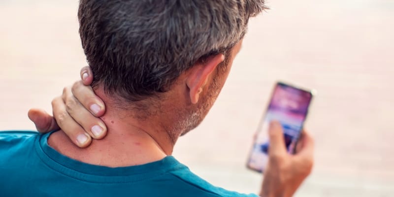 A man experiencing neck pain, a key symptom of text neck syndrome, looking down his smart phone.