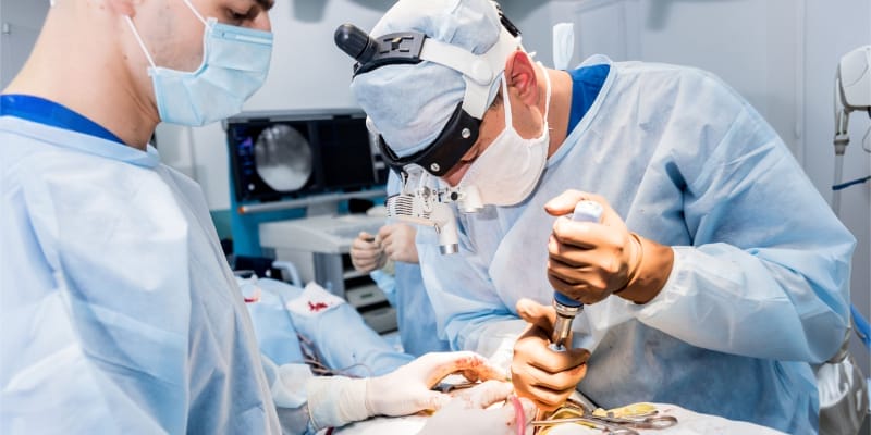 Surgeons performing spinal laminectomy in operating room with surgical equipment